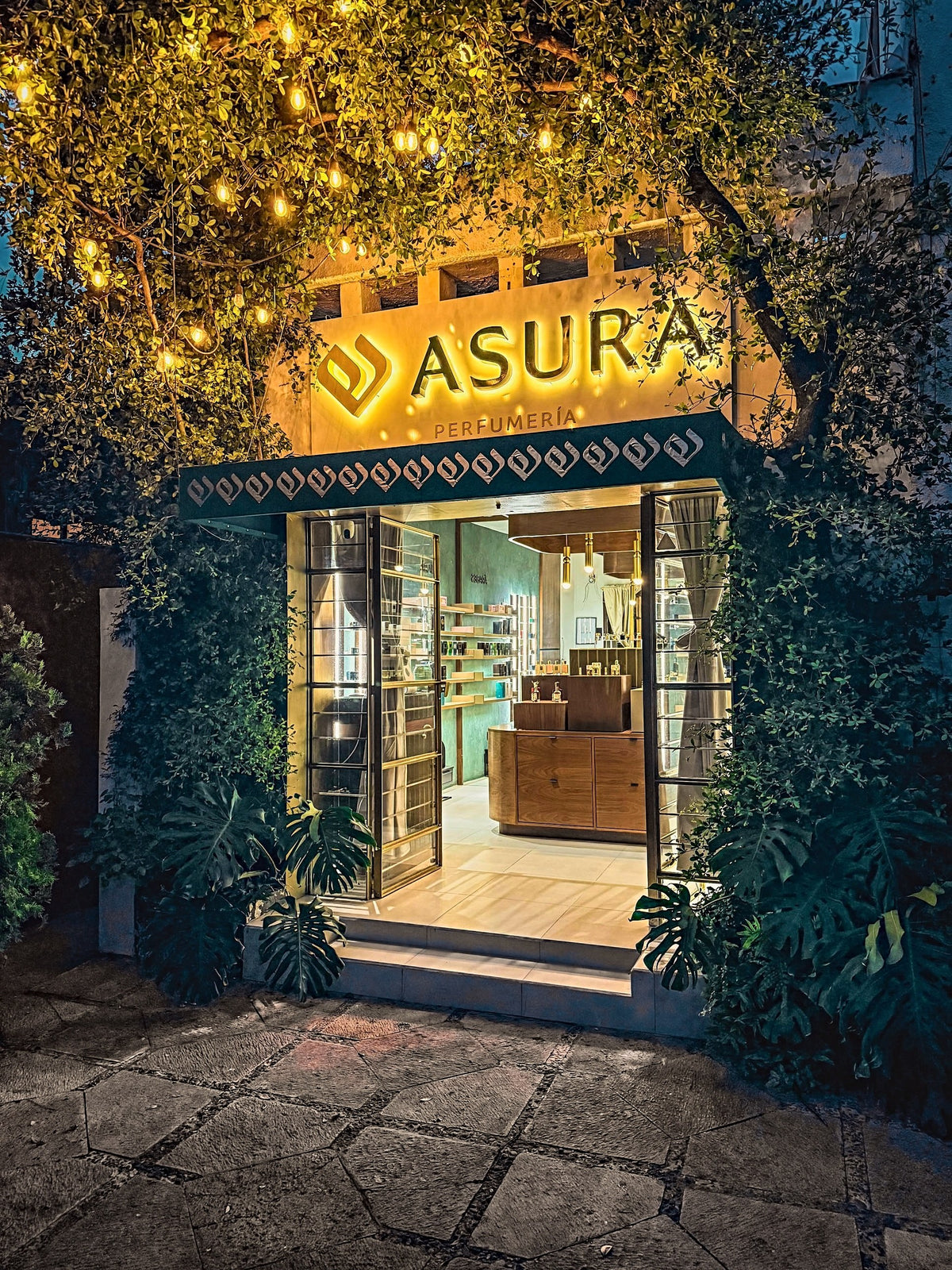 Fachada de ASURA Perfumería de noche, con el letrero encendido y las puertas abiertas